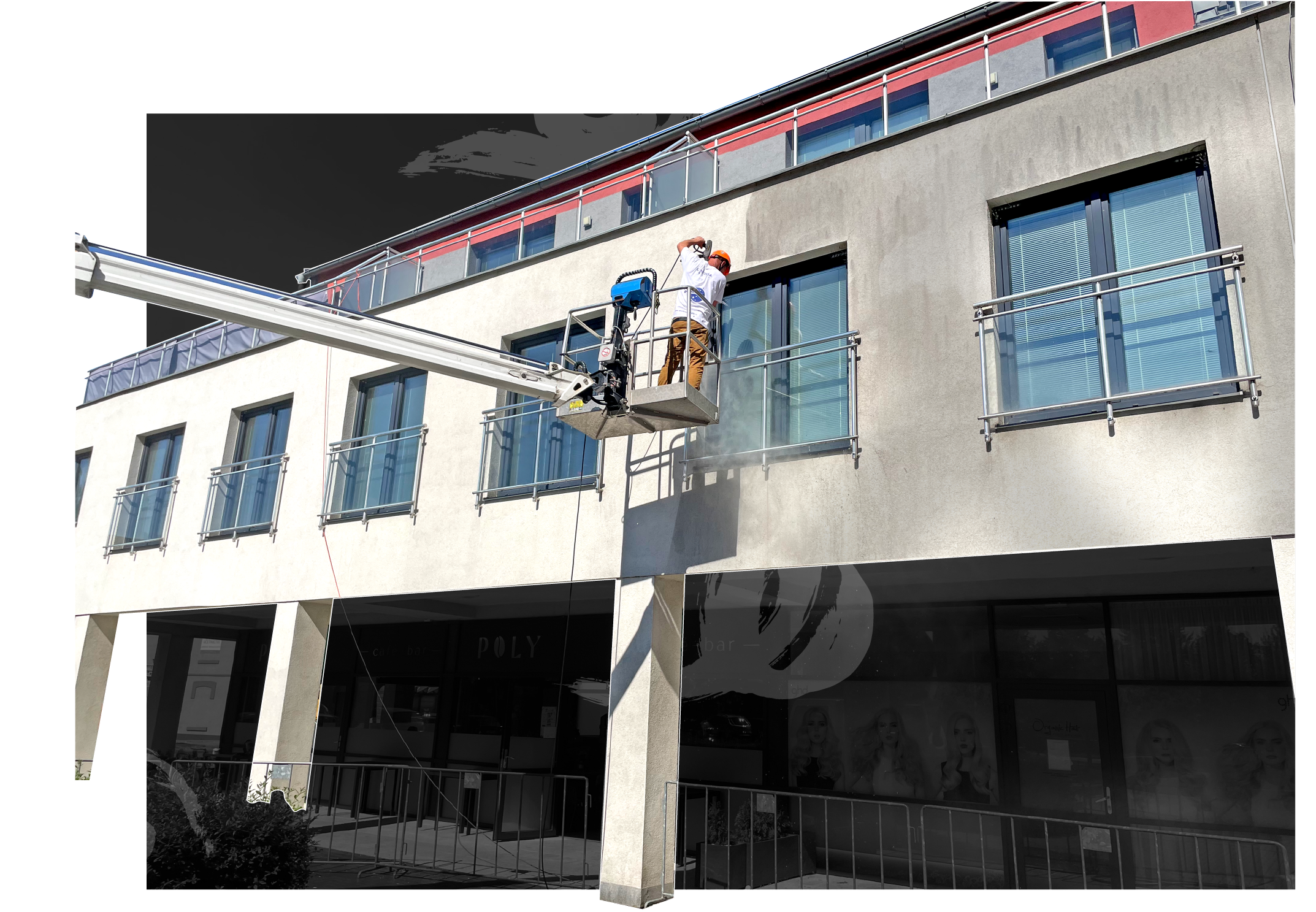 Worker wearing a helmet pressure washing windows on the second floor of a modern building using a lift.