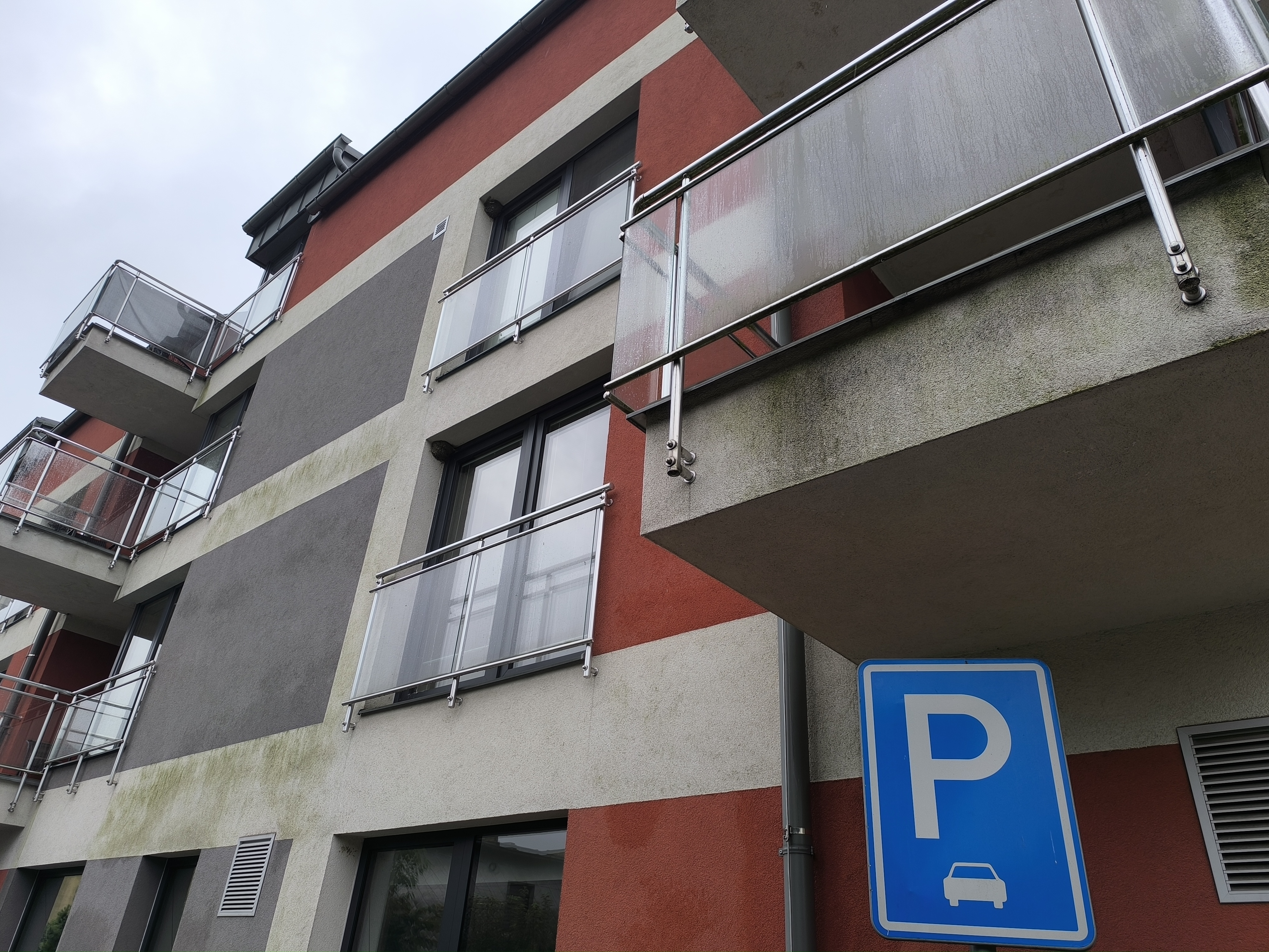 Modern apartment building with balconies and a blue parking sign in the foreground.
