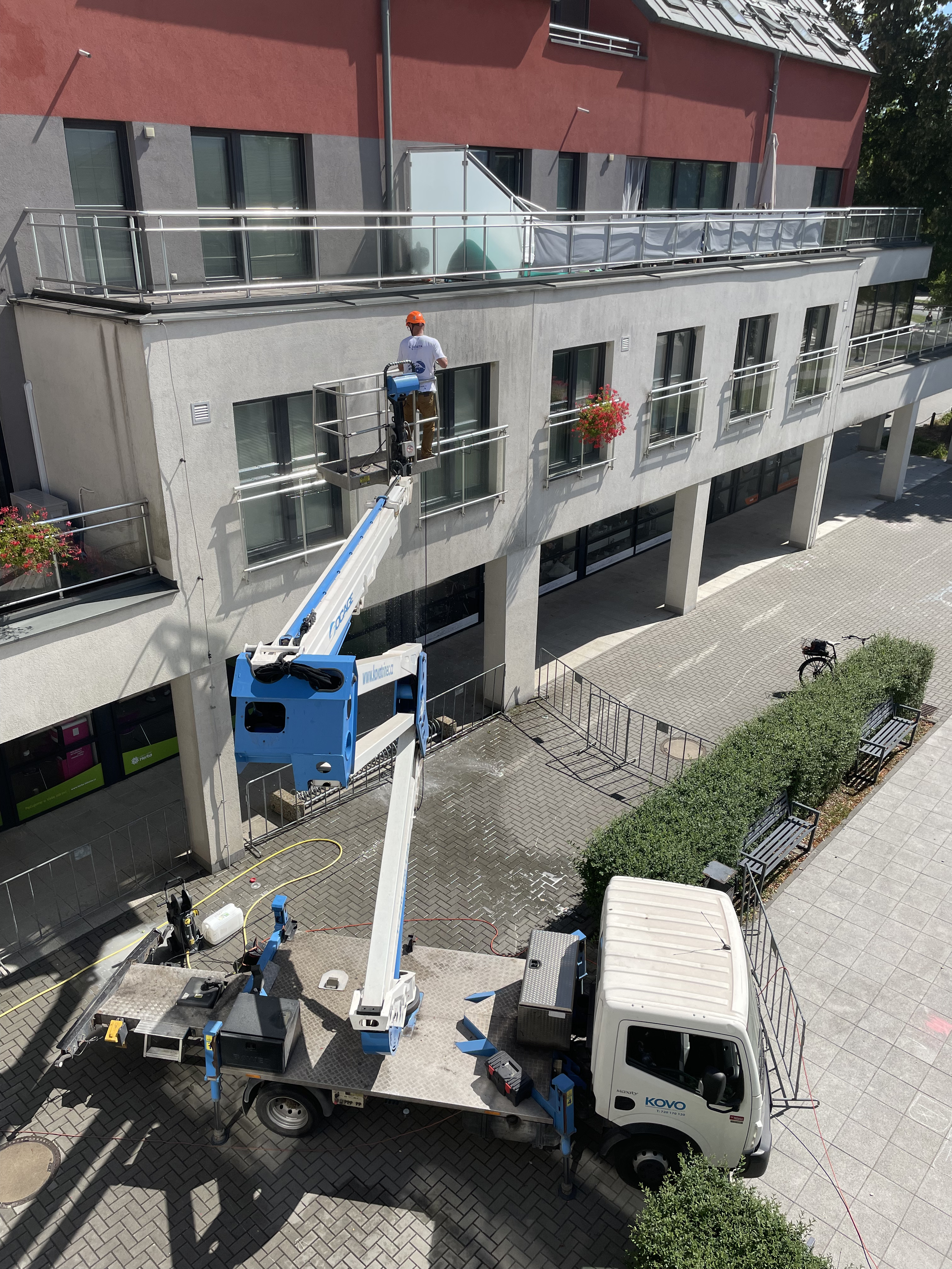 Worker wearing an orange helmet on a blue and white aerial lift cleaning windows on a modern apartment building.