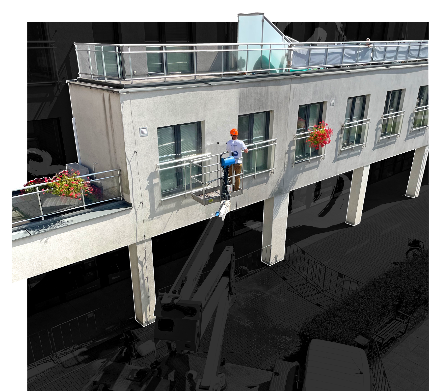 Worker wearing an orange safety helmet cleaning windows on a white building facade using a pressurized water tool from a hydraulic lift.