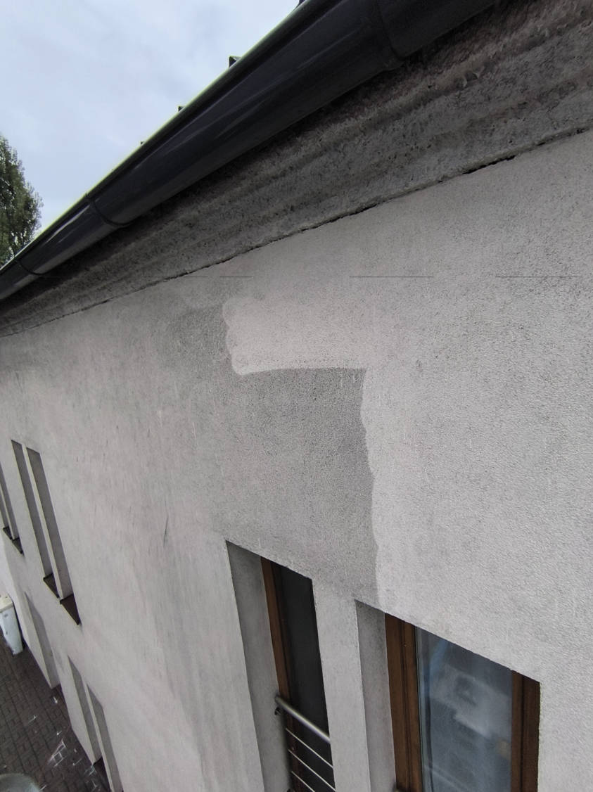 Exterior wall of a building showing a patch of freshly applied lighter paint above two narrow windows under a black gutter.